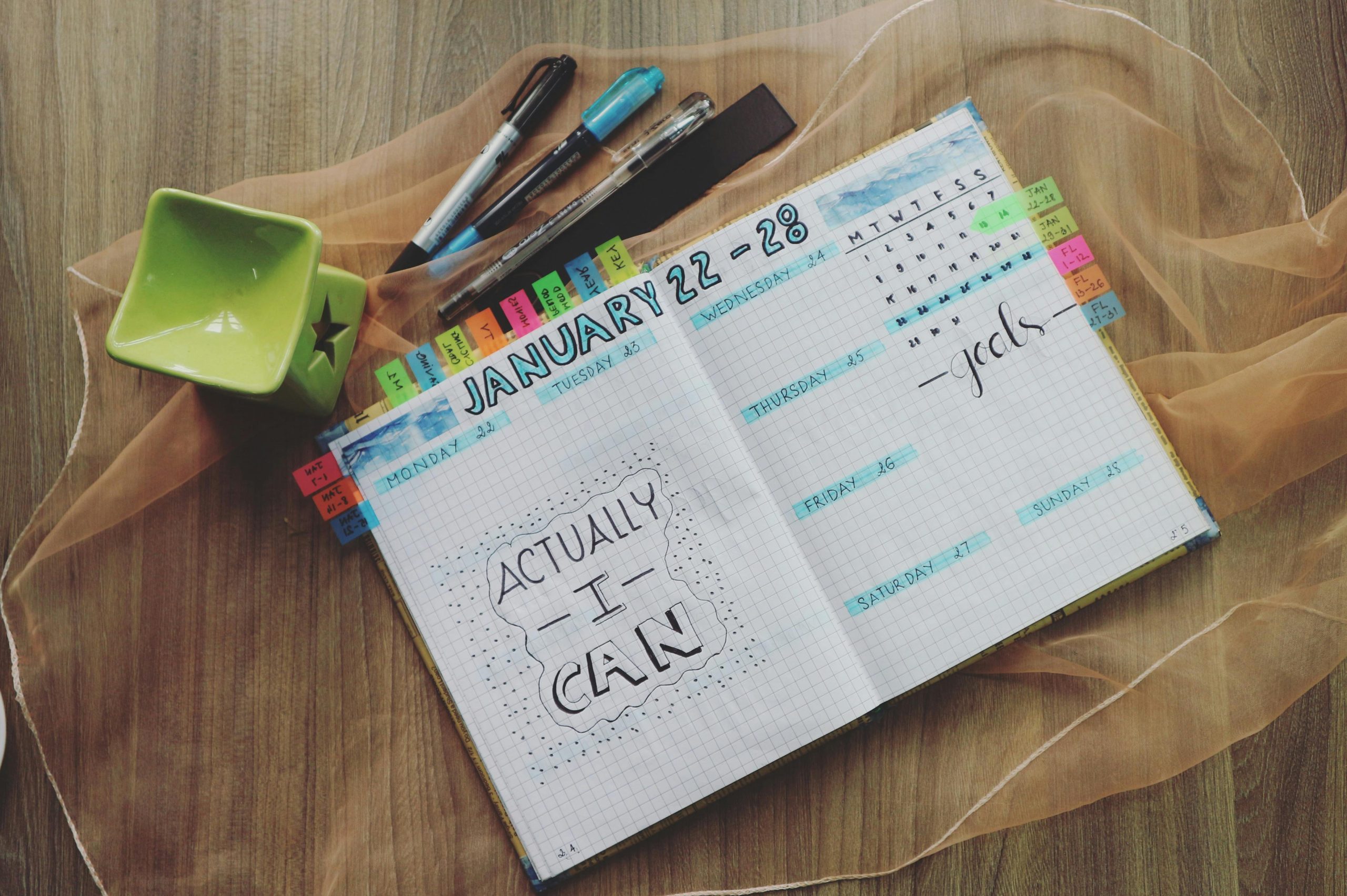 Open planner with motivational quote and colorful tabs on wooden desk.